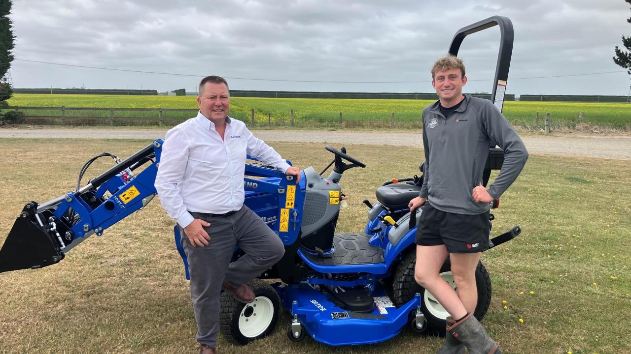 Two people standing in a field next to a blue tractor