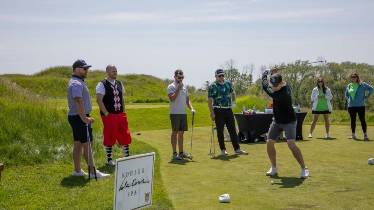 People standing on a green watching someone golfing
