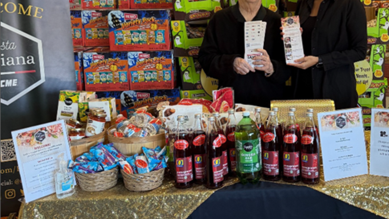 A person and person standing next to a table with food items