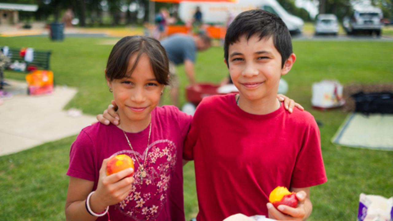 Two children holding fruit and posing