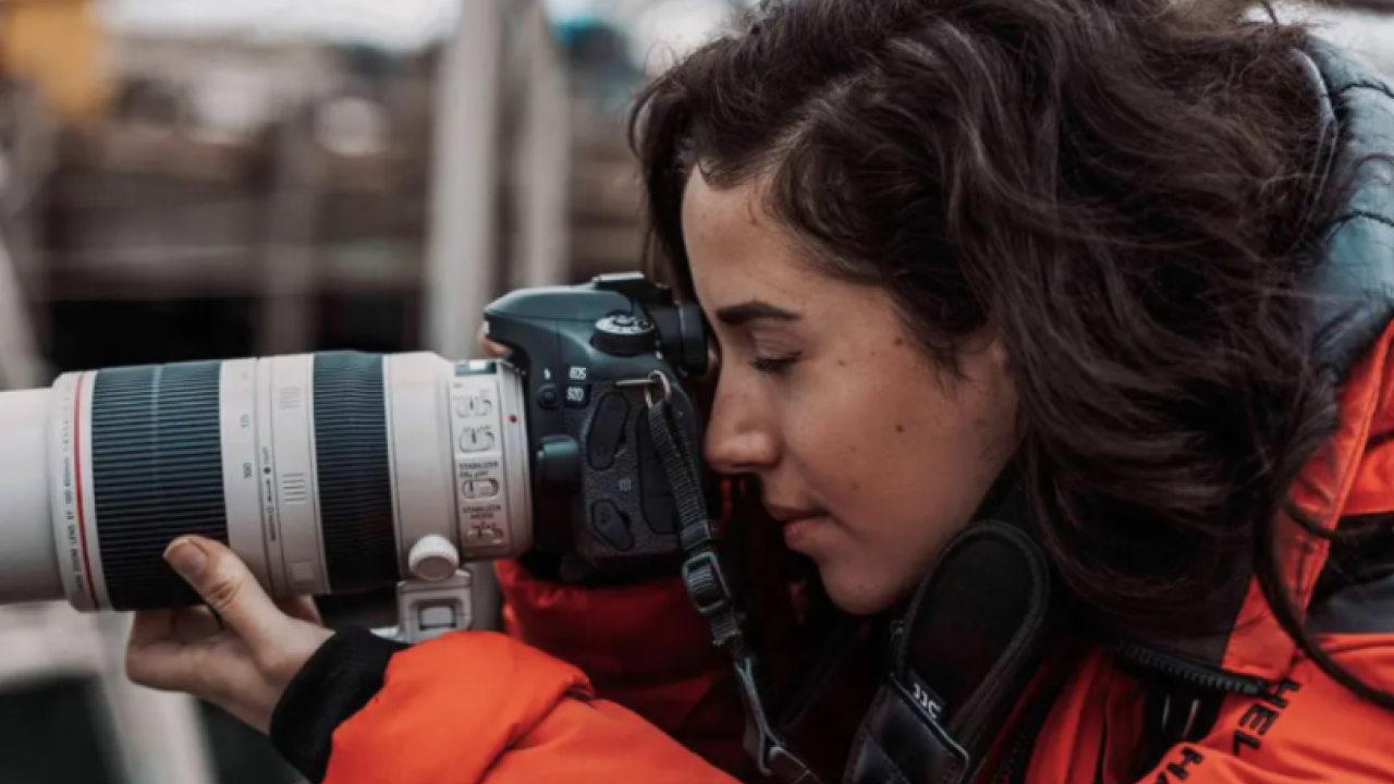 Brunette woman in orange jacket holding a camera
