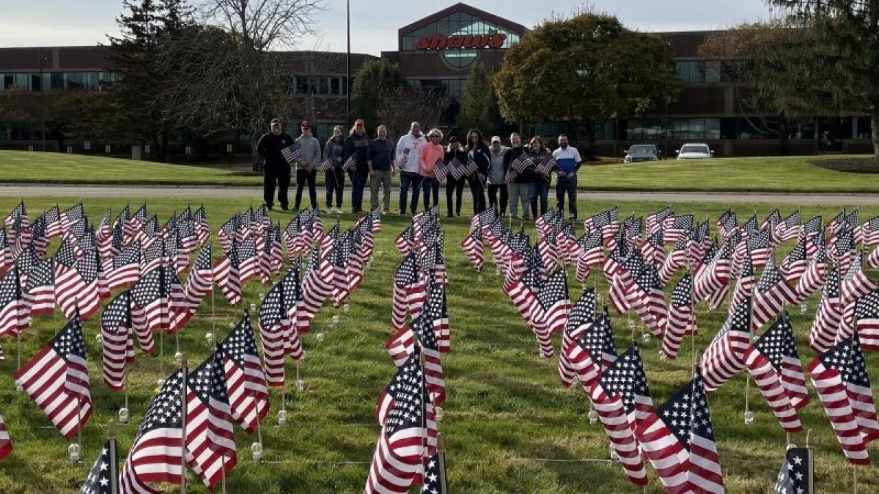 Group of people posing behind field with flags in front of Albertsons Cos' Shaw's Store Support Center Sign