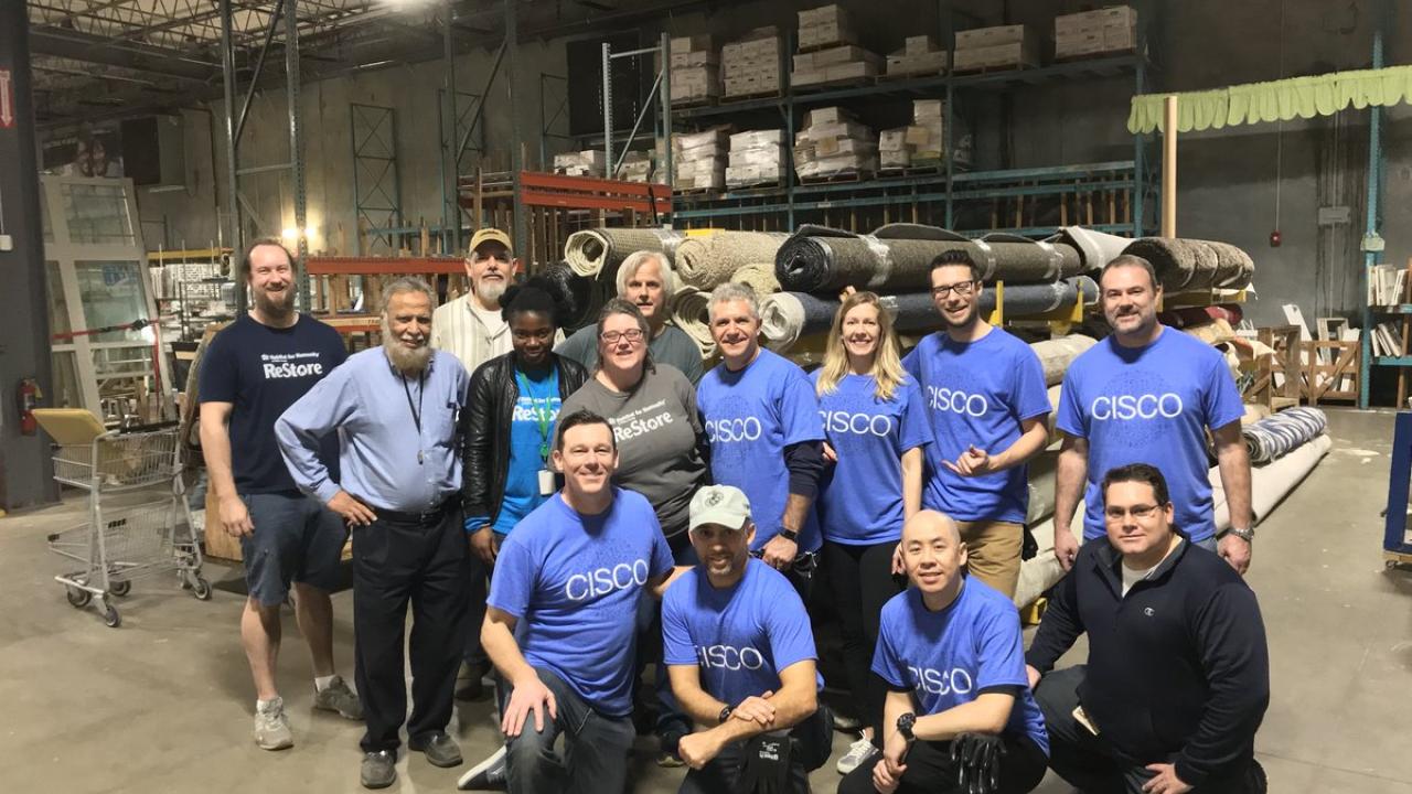 A group of people posed in a warehouse, many wearing matching Cisco t-shirts.