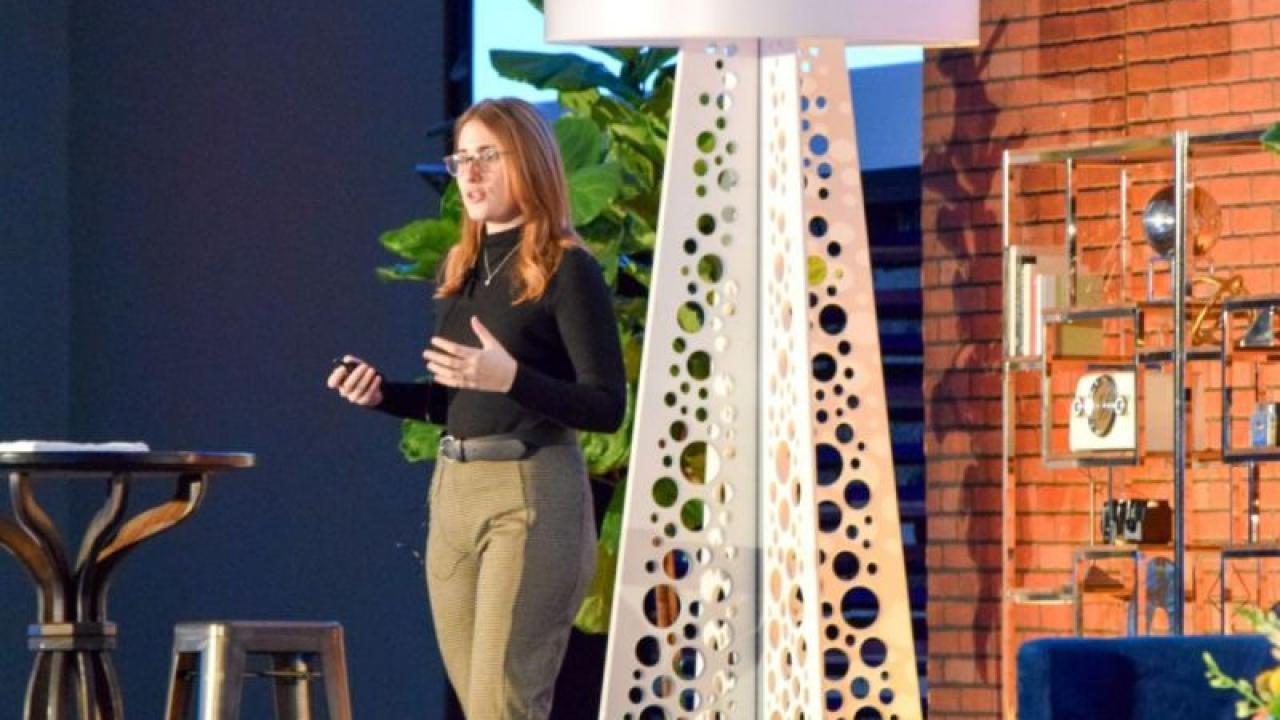 Sara Lanning standing on stage with various furniture and plants around her
