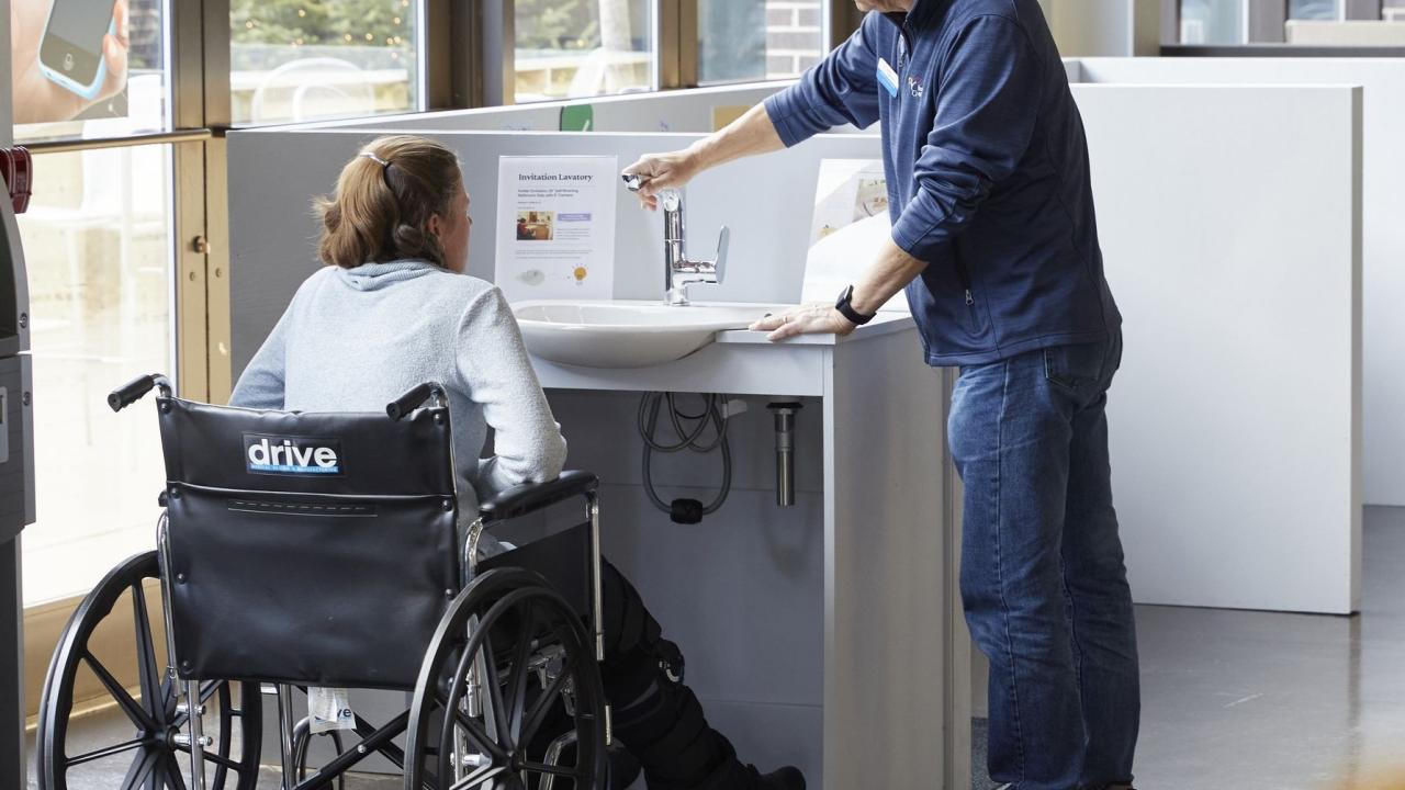 Woman in wheelchair being shown an accessible sink by a standing man