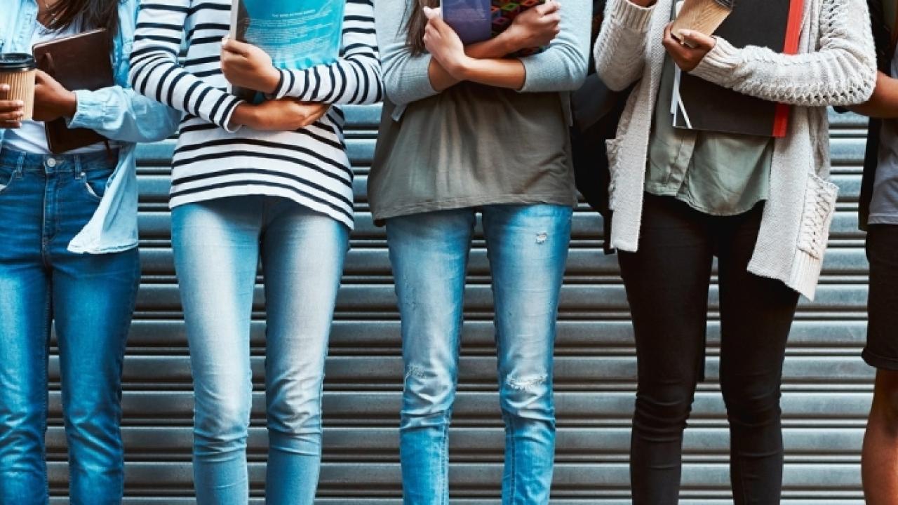 legs and bodies of people wearing jeans, t-shirts, sweaters and shorts, holding phones and coffee cups