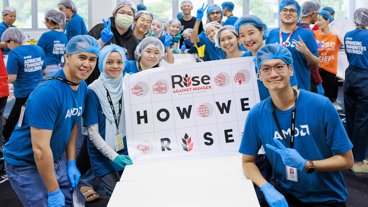 People in AMD t-shirts, gloves and hair nets posing for the camera with a sign that says: "How We Rise"