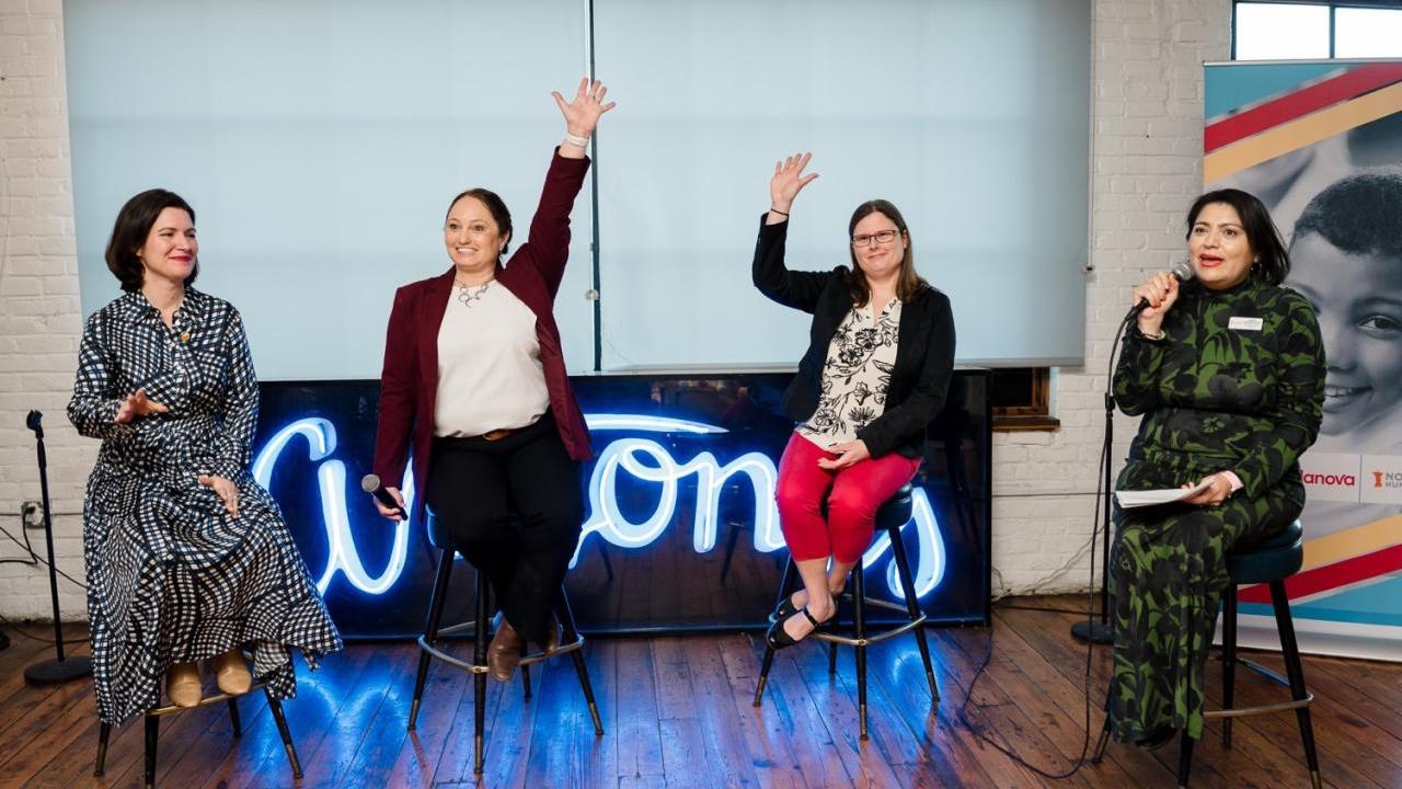 A group of women sitting on stools with their hands up