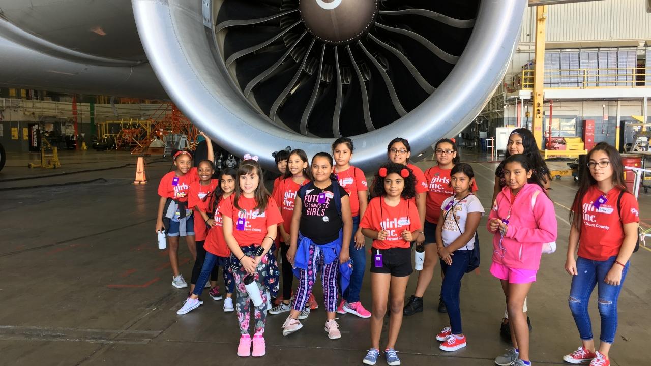 Class of girls in front of jet engine