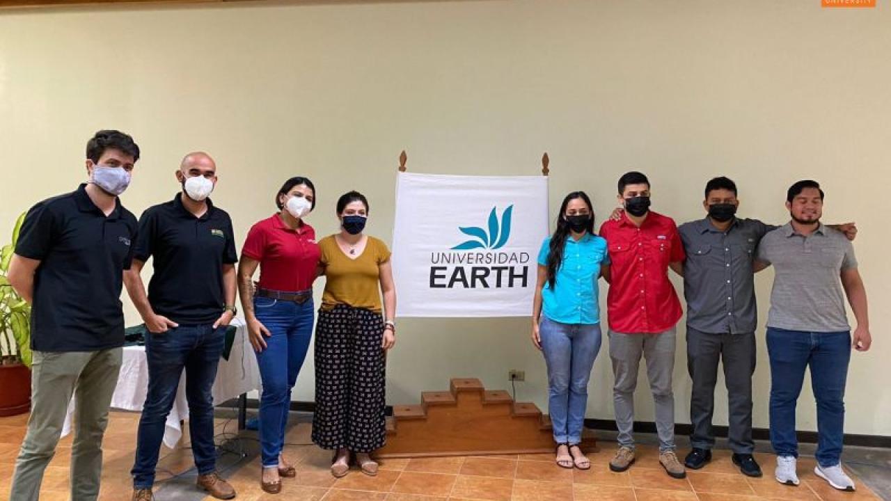 8 people stand in between a Universidad Earth banner.