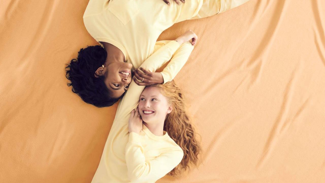 Two models wearing yellow Comfort Colors clothing, lying against a yellow backdrop