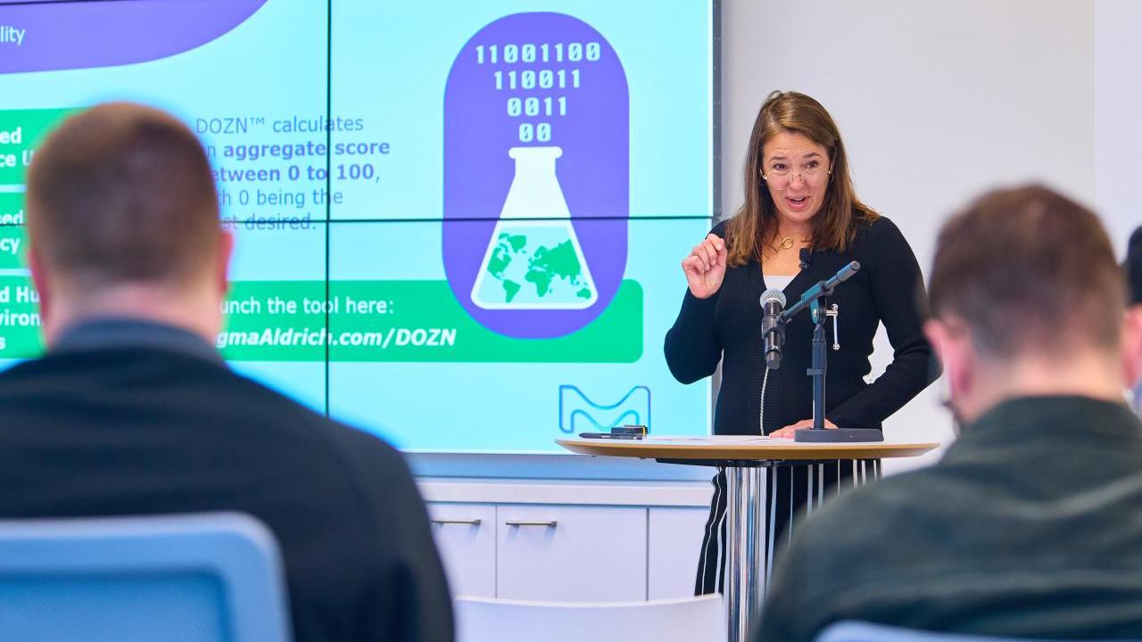 Woman standing at podium presents on "Green Chemistry" to an audience. 