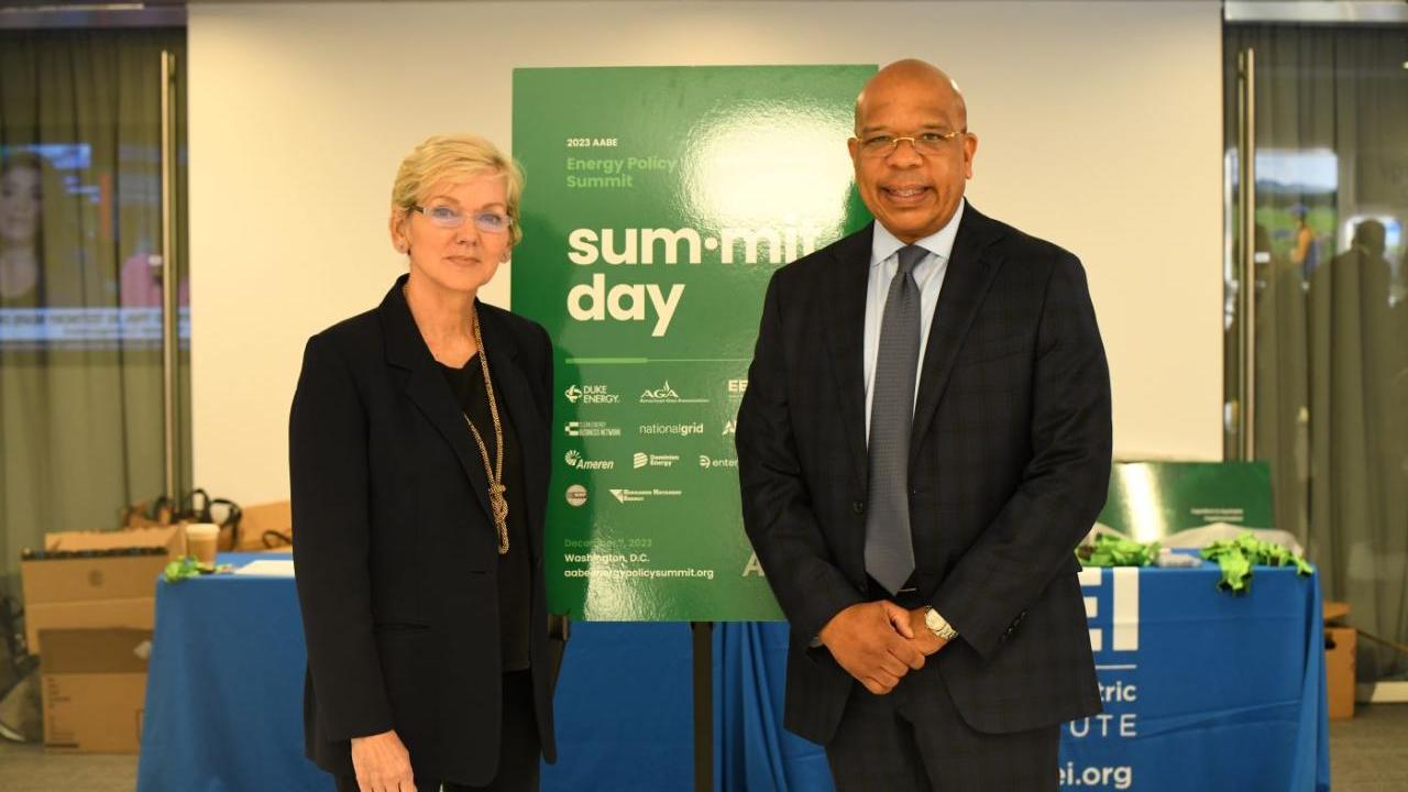 2 people in front of AABE Energy Policy Summit poster