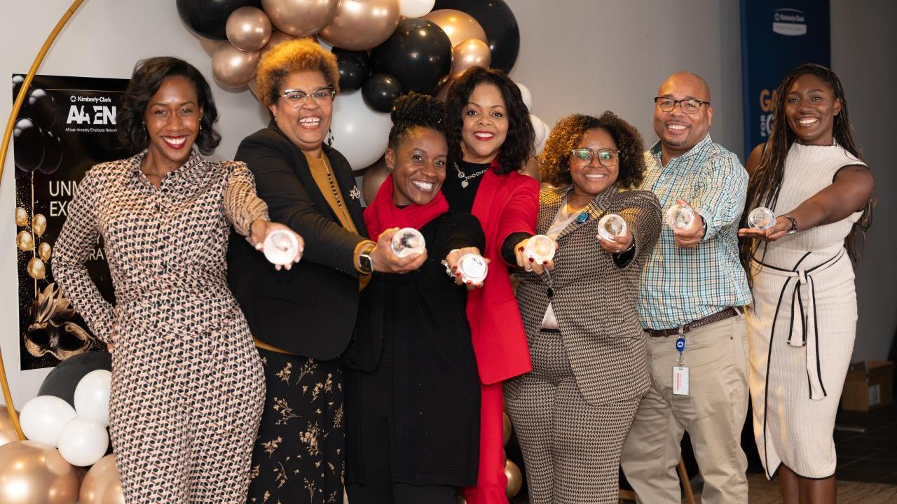 A line of smiling people posed, each holding out a round object.