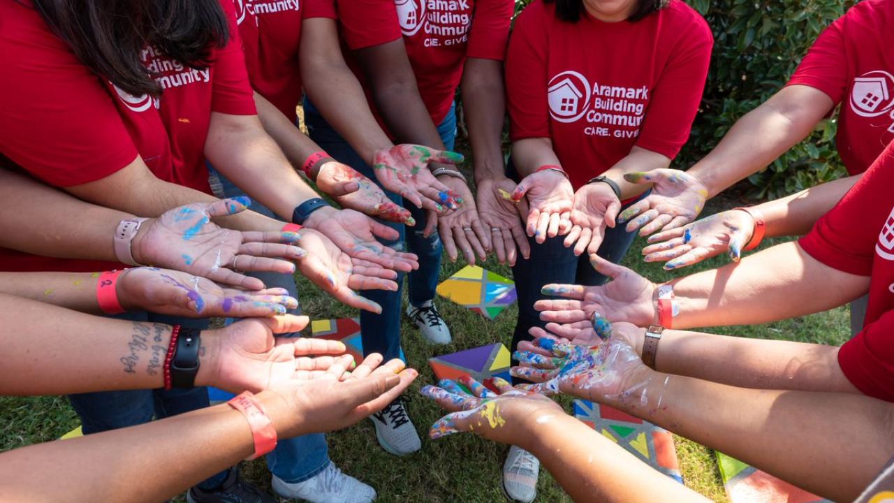 Aramark volunteers display their paint-covered hands in a circle outside
