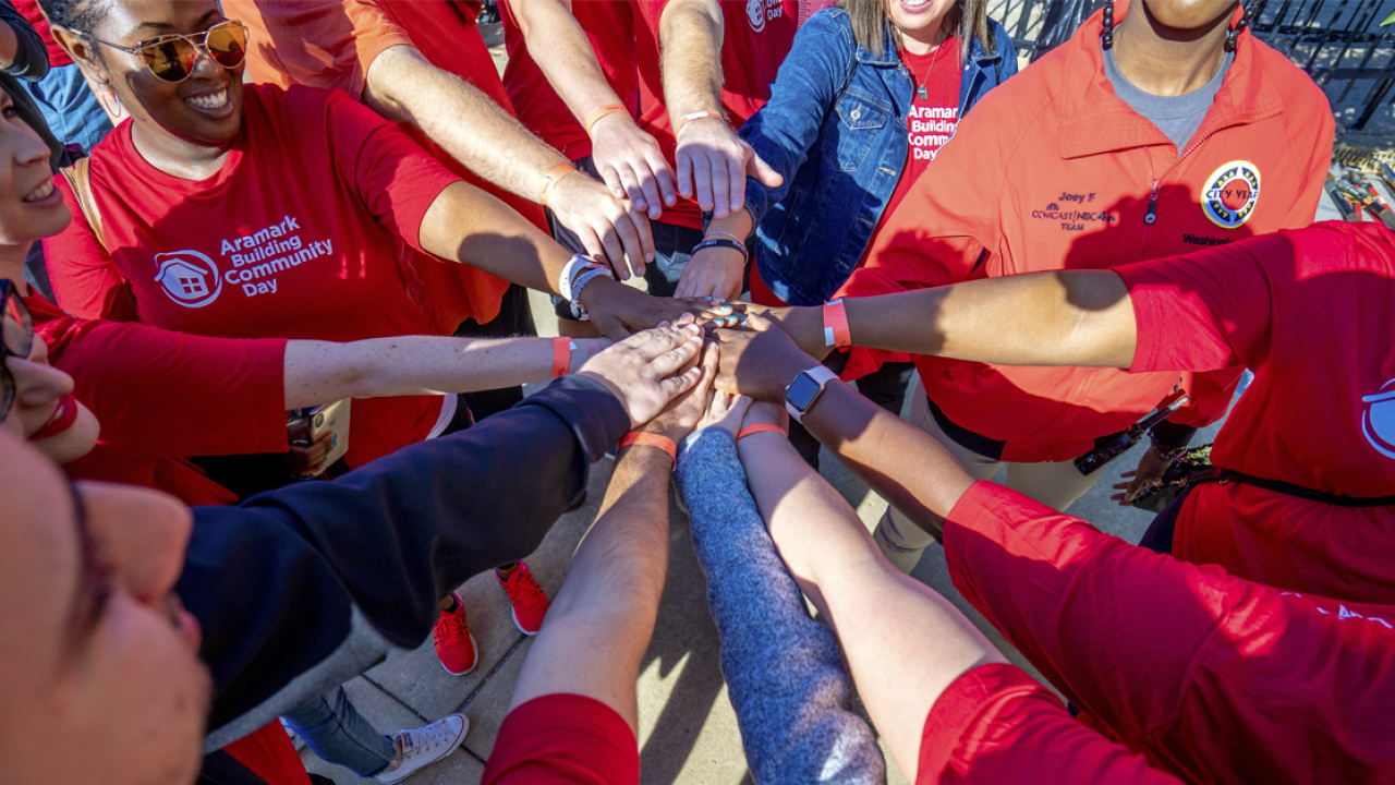 Aramark volunteers join their hands together in the center of a circle as part of a team huddle
