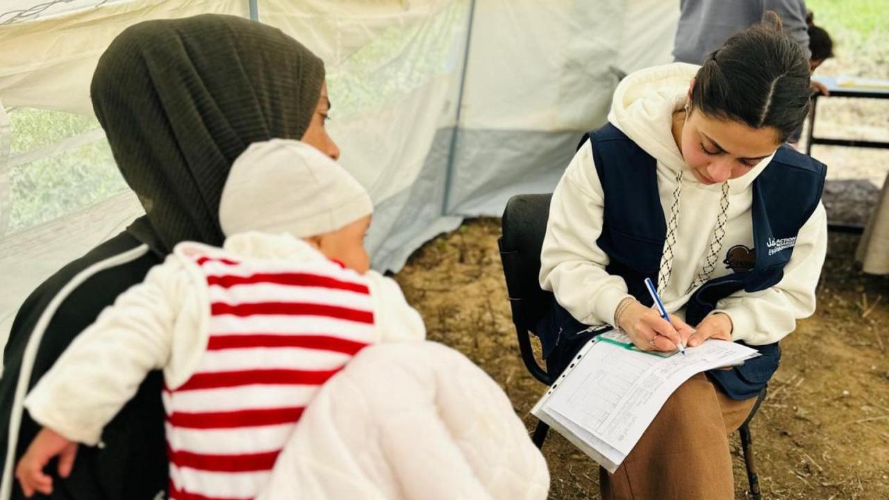 Woman holds baby while being assessed by an Action Against Hunger staff member. 