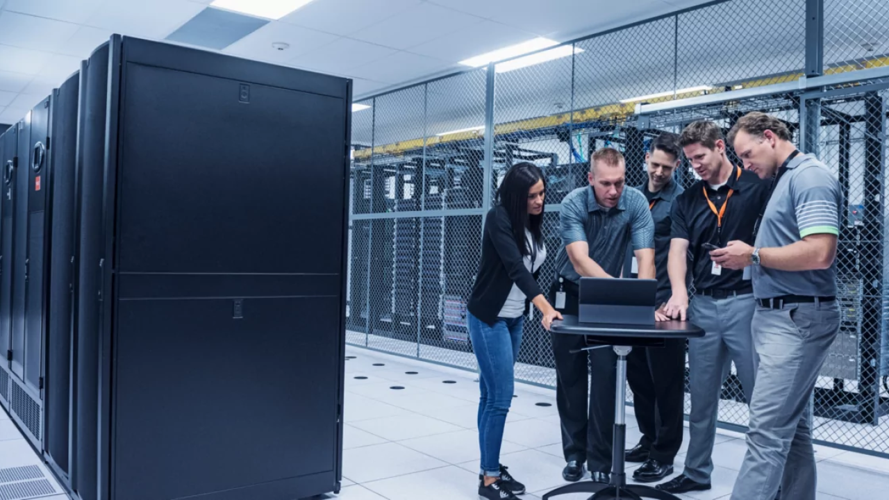 5 people looking at a laptop around servers