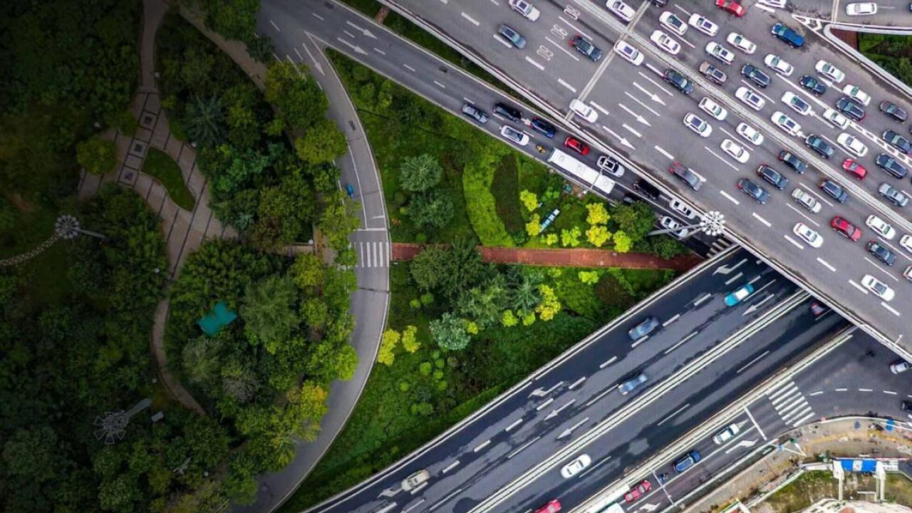 Aerial view of intersecting highways and traffic. An area of trees and grass are central and to the left side.