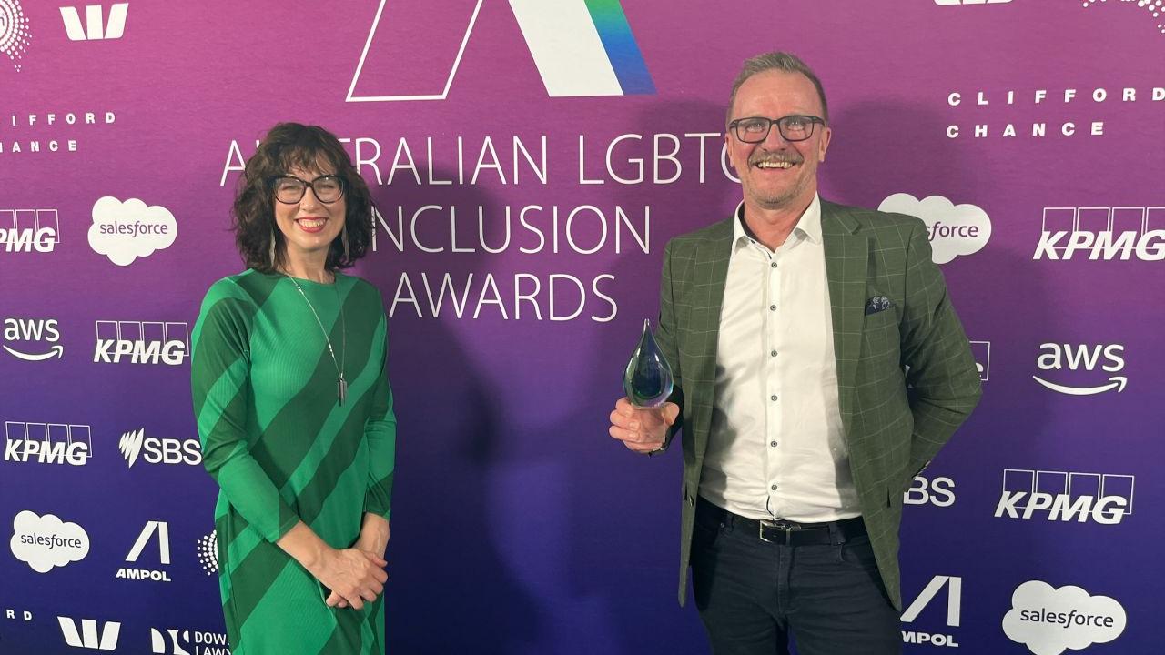 Two people stood in front of an Australian LGBTQ Inclusion Awards event back drop 