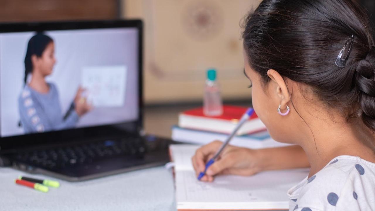 student writes in a notebook while watching a laptop screen