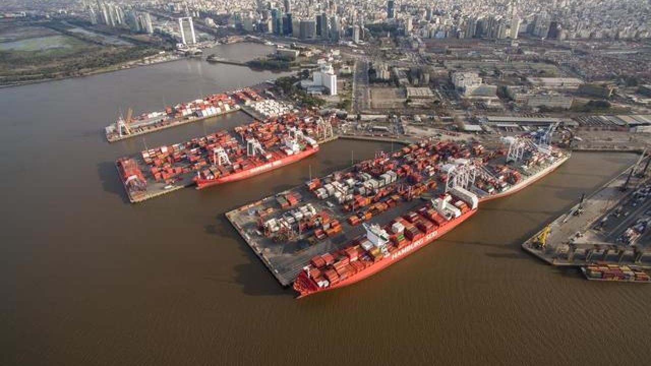 Aerial view of DP World’s Buenos Aires terminal on the Río de la Plata, showing container ships docked at the port with the city skyline in the background.
