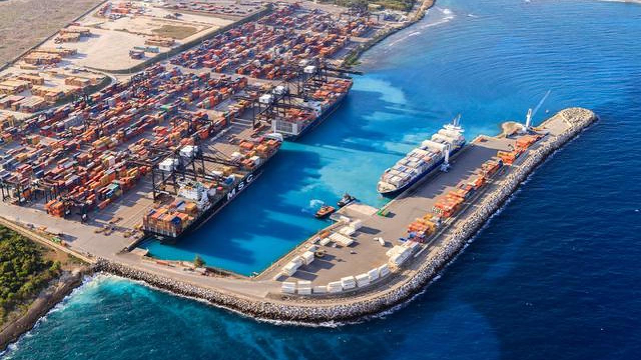 Aerial view of DP World’s Port of Caucedo in the Dominican Republic, showing container ships docked at the terminal, cranes loading cargo, and stacked shipping containers along the turquoise Caribbean coastline.