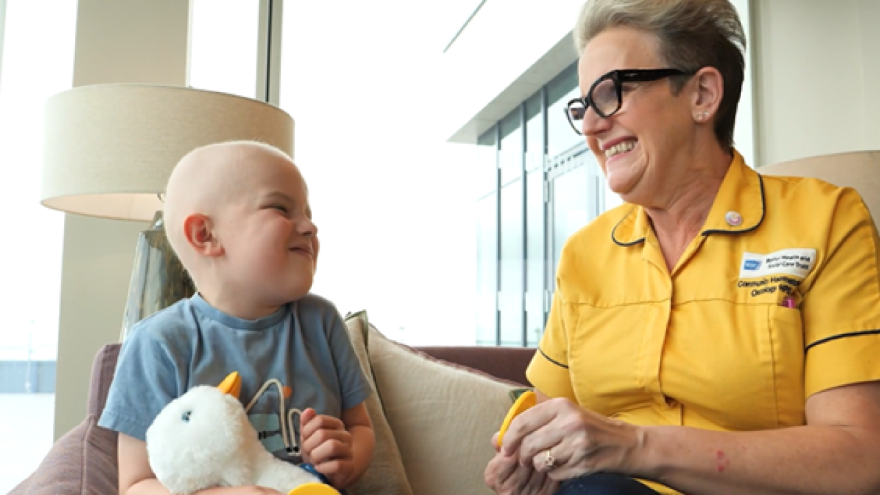 Young cancer patient holding the Aflac Duck and seated with a health professional.