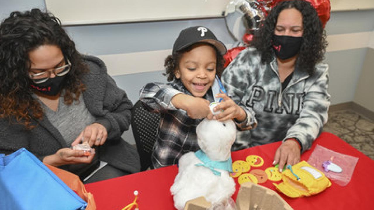 Child seated with two adults receives an Aflac My Special Duck.