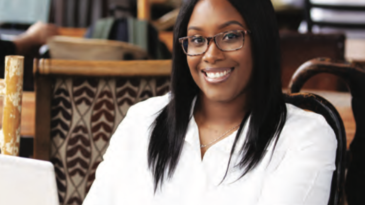 African American female, smiling, at work behind a laptop.