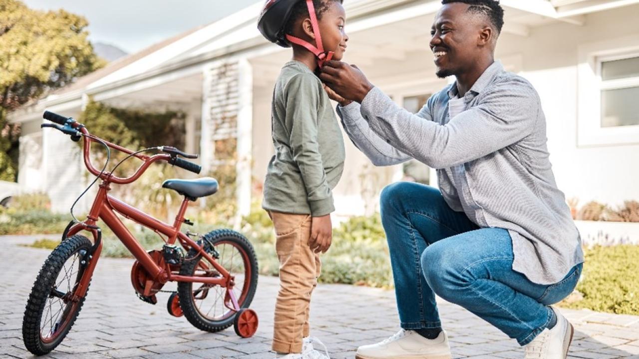 A father helping his son put on his bicycling helmet.