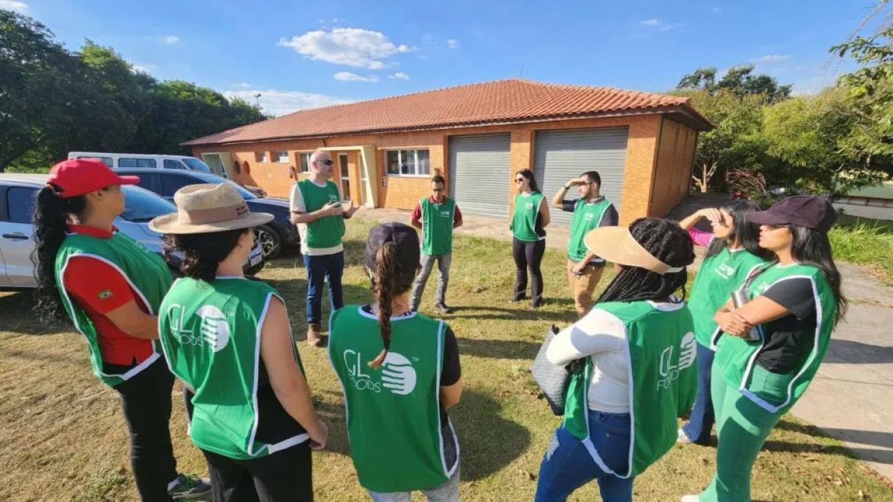 Students and adults in matching green vests meet in a circle outside a building in a rural area.