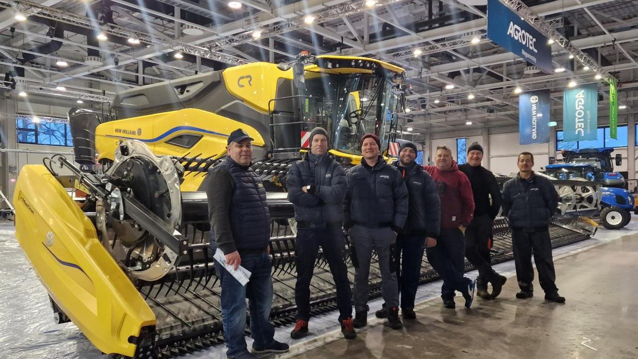 A group of people stood in front of yellow agricultural machinery 