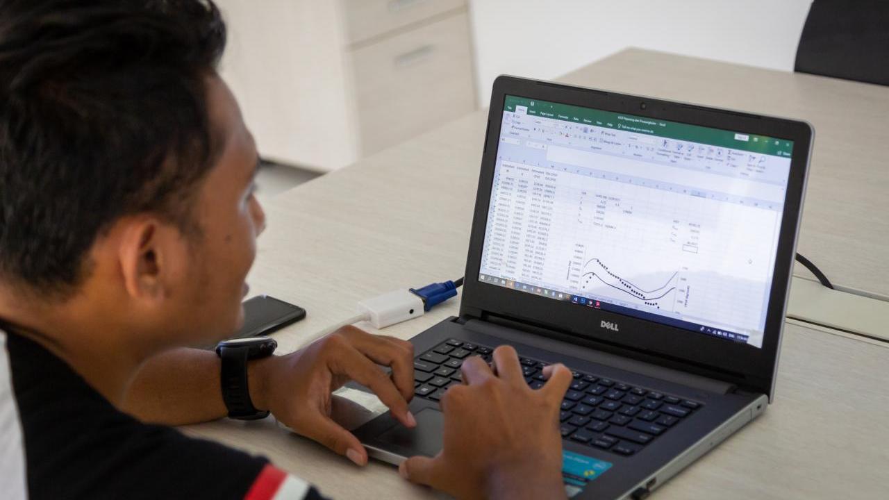 A person looking at a laptop screen. Graphs, spreadsheets visible.