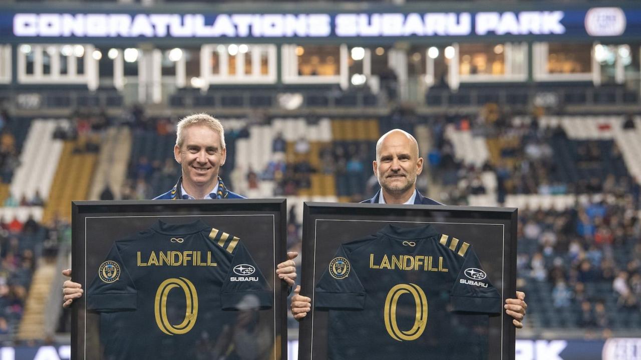 Two people holding up soccer jerseys with the words "Landfill 0"