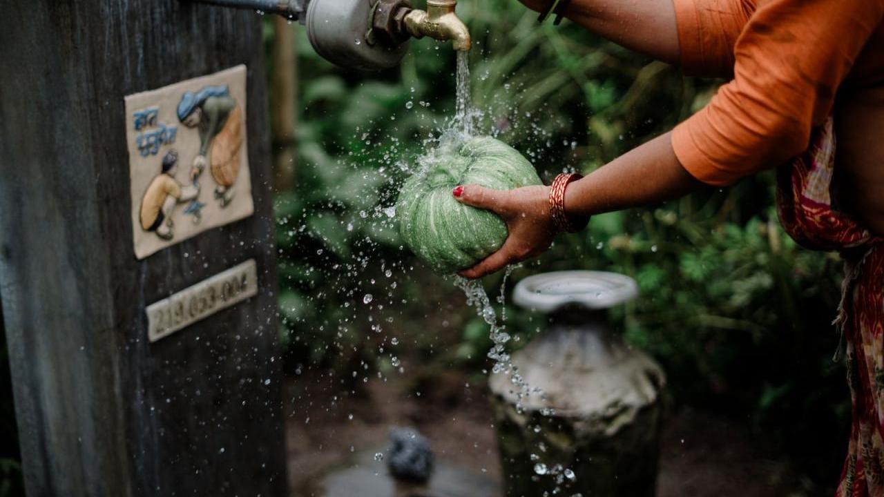 A woman uses a water well to wash a vegetable in Nepal