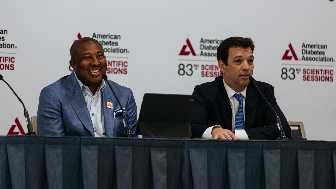 Two people seated at a table with microphones in front of backdrop with American Diabetes Association logo