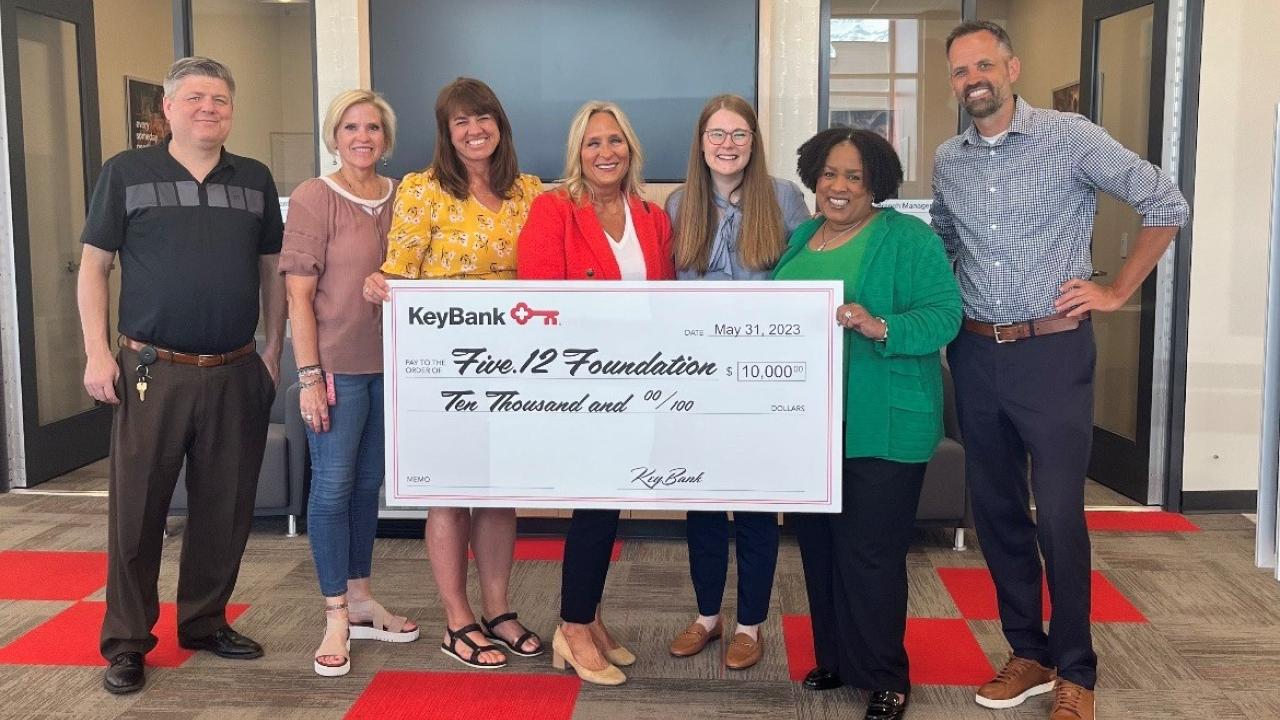 Seven people holding up large check for $10,000 donation to the Five.12 Foundation