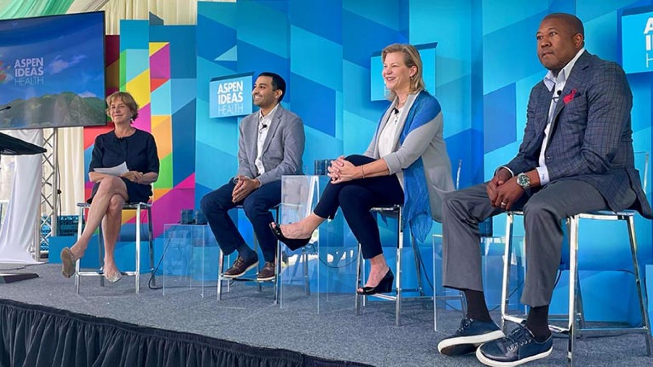 Four people on stage seated. Aspen Ideas Health on many screens behind them