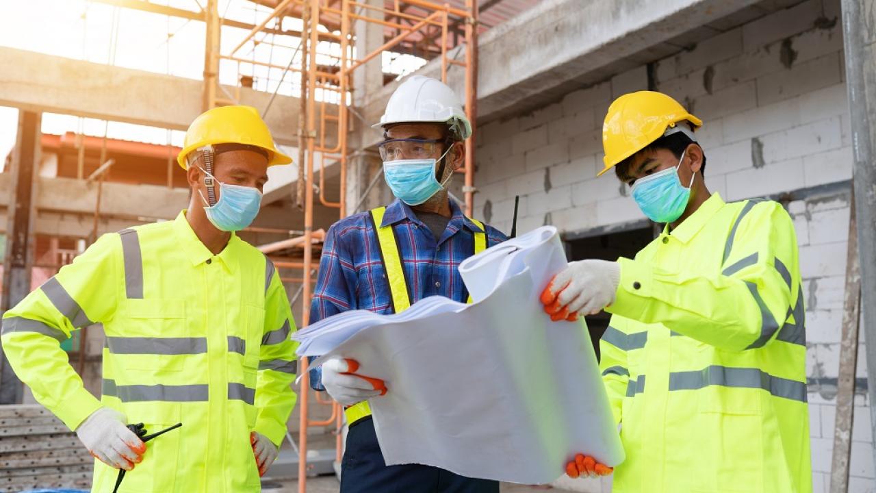 three workers looking at a large plan on paper