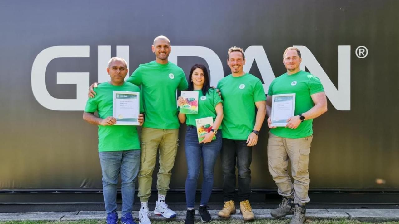 Five mental health first aid certified employees from Gildan Australia posing with their certificates in front of a Gildan logo