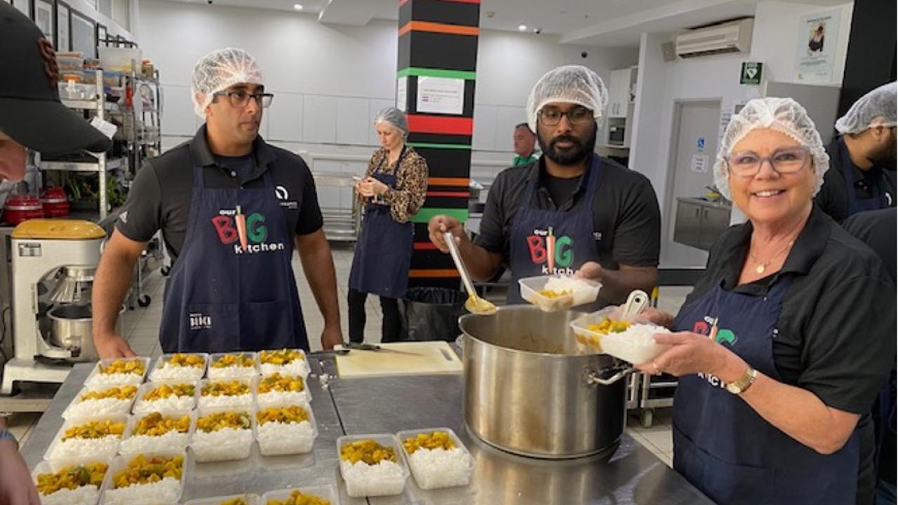 Group of volunteers in a kitchen, wearing hair nets and aprons with "Big Kitchen" on them.