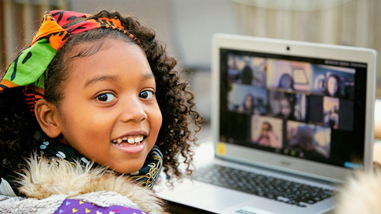 Young black student seated in front of a laptop smiling.