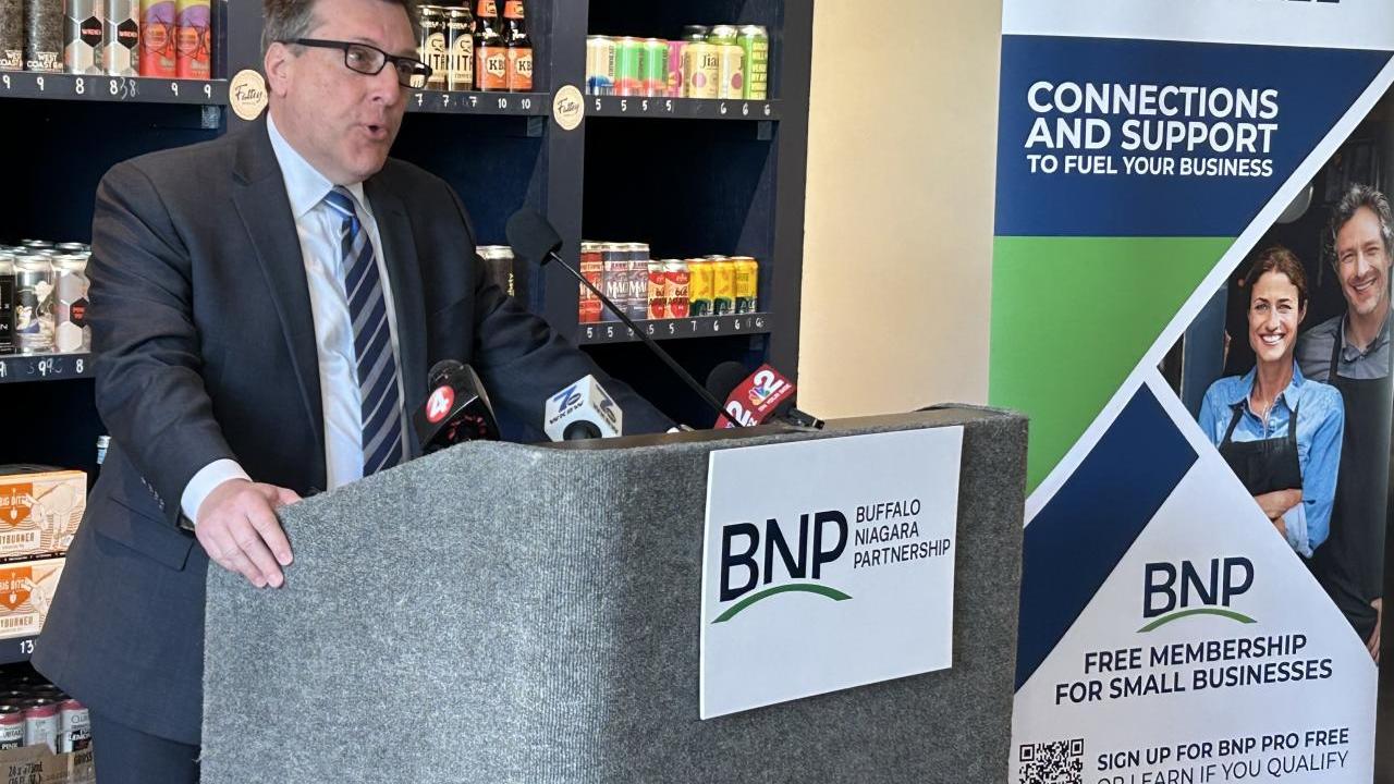 A person stood giving a speech in front of product shelves  