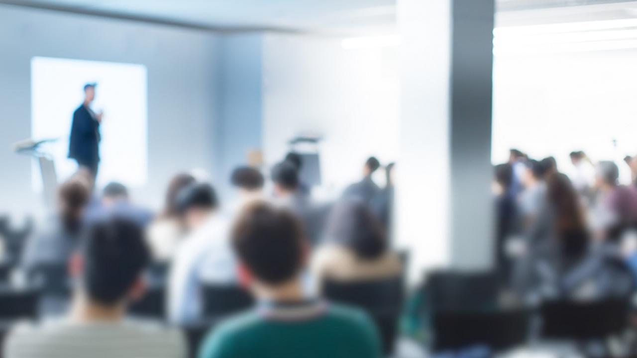 blurry representation of a speaker on a podium in front of audience