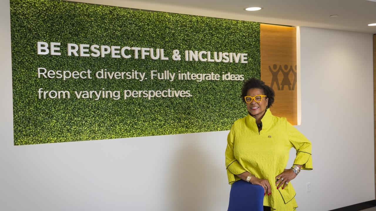 Person standing in front of a sign reading, "Be respectful & inclusive: Respect diversity. Fully integrate ideas from varying perspectives."