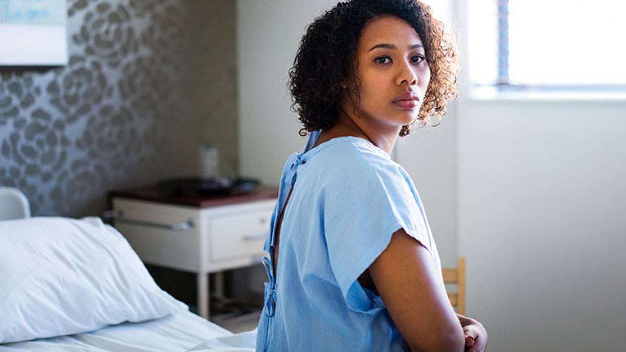 Patient in hospital gown sitting on a bed, turning to look behind her