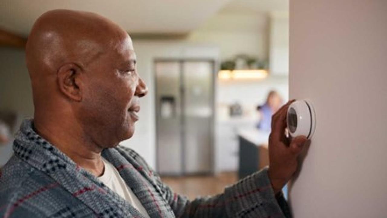 A person in a robe adjusting a thermostat in a home setting.