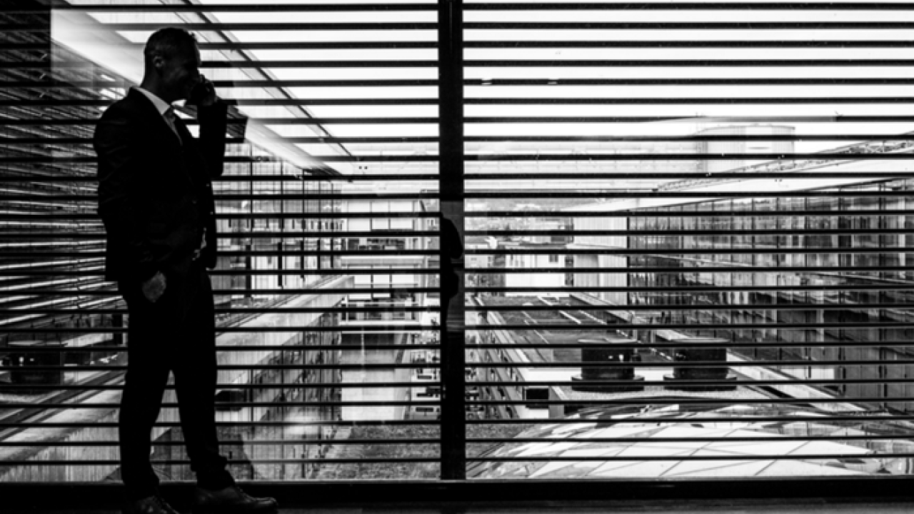 black and white representation of a businessman in front of a large window with blinds open 