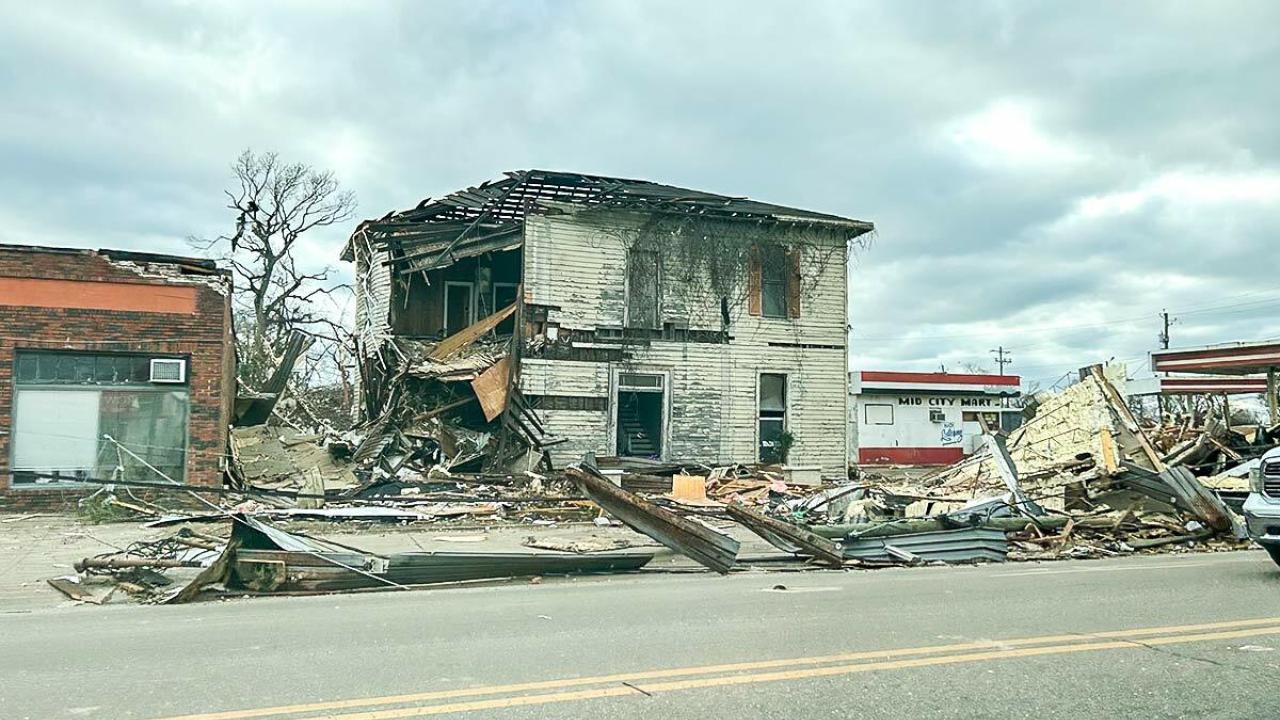 Street view of building damaged by a tornado, debris strewn around the street.